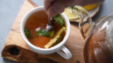 Limonlu ve naneli çay. El, bitki çayını kaşıkla karıştırıyor. Sağlıklı sıcak içecek.