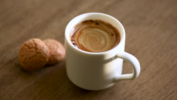背景にコーヒーエスプレッソとカリカリのアマレッティクッキーの蒸しカップ 木製のテーブルの背景 朝の習慣 目を覚ます儀式の概念 — ストック動画