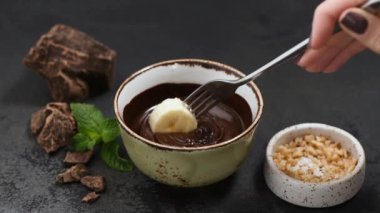 Muzu erimiş siyah çikolataya batırmak ve ezilmiş fındıklara sarmak. Sağlıklı atıştırmalıklar. Çikolata fondü konsepti