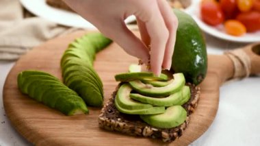 Avokado sandviçi. Kadının eli sağlıklı avokado ve çavdar ekmeğinin üstüne lahana ve tohum ekliyor. Vejetaryen, vejetaryen gıda konsepti