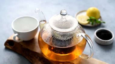 Bir fincana siyah çay dolduran kişi. Taze demlenmiş limon ve nane yaprağıyla demlenmiş çay demliği.