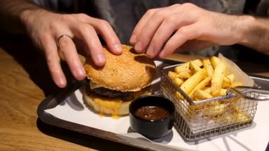 Erkek Eller Burger Restaurant 'ta servis masasından hamburger alıyor. Fast Food Cheeseburger ve patates kızartması yiyorum. 4k Görüntü