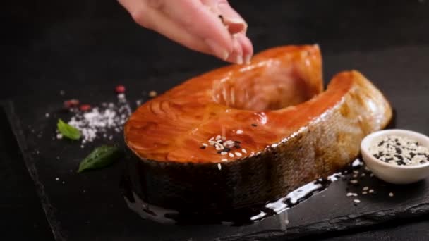 黒いスレートの背景にゴマと季節の照り焼きサーモンの遅い動き アジア料理料理 — ストック動画