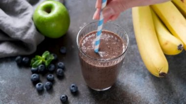 Sağlıklı çiğ meyve ve çikolatalı protein karışımı. Kadın eli bardakta kokteyl karıştırıyor kağıt kokteyl çubuğuyla. Sağlıklı fitness vegan yaşam tarzı konsepti