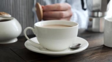 Kişi sütlü bir fincan kahveye şeker ekler. Ahşap masa arka planı. Sabah kahvesi.
