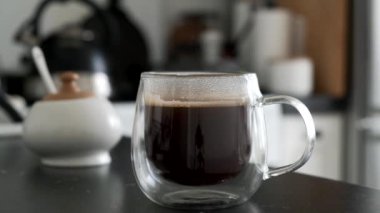 Mermer mutfak masasında, cam bardakta sıcak, sade kahve. 4K görüntü