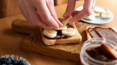 Kadın muzlu çikolatalı fındıklı tost hazırlıyor. Sağlıklı vejetaryen kahvaltısı, öğle yemeği veya tatlı atıştırmalık.