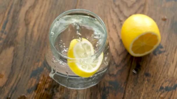 ガラスのレモンできれいな水 レモンスライスの動きが遅い水のガラスに落ちる 健康的な朝のドリンクルーチン — ストック動画
