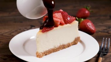 Çikolata soslu cheesecake. Çilekle süslenmiş klasik New York peynirli kekinin üzerine çikolata sosu dökülüyor.