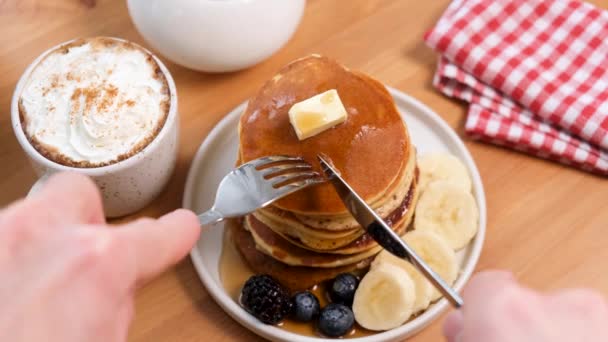 シロップとバターのパンケーキと朝食のためのクリームとシナモンとコーヒーカップ フォークとナイフでパンケーキを食べる アメリカの朝食 — ストック動画