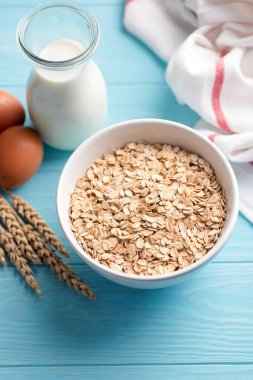 Mavi ahşap masa arkasında yulaf gevreği ve süt şişesi. Yulaf ezmesi veya sağlıklı yulaf kurabiyesi pişirmek için gerekli malzemeler.
