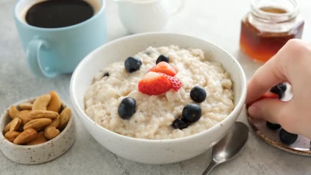 健康的な朝食食品を食べる オートミール粥に新鮮な夏の果実を追加します 黒コーヒー オートミールとベリーのボウルと朝食テーブル — ストック動画