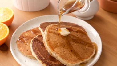 Amerikan gözlemelerinin üzerine tereyağlı şurup dökülüyor. Tahta bir masanın üzerinde leziz, tatlı kahvaltı krepleri.