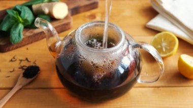 Zencefilli limonlu siyah çay demlemek ve cam çaydanlıkta nane şekeri, ahşap masa arkaplanı. Sağlıklı bitkisel çay grip önleyici ve bağışıklık arttırıcı