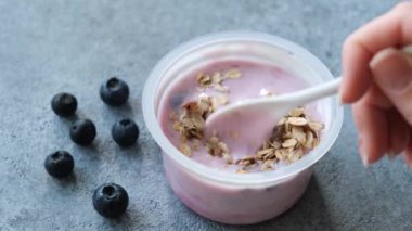 Plastik kavanozda müsli yabanmersinli yoğurt. Müsli ile Yunan yoğurdu yemek. Bir kaşık yaban mersinli yoğurt alıyorum.