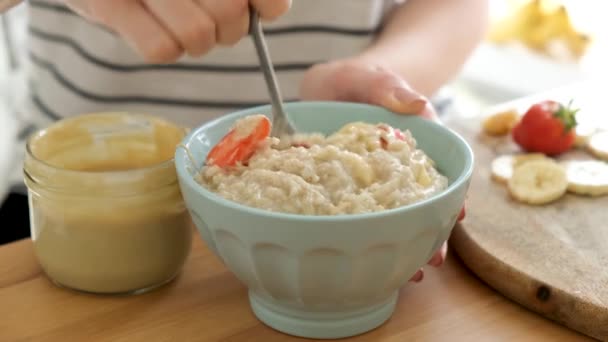 在碗里搅拌燕麦粥 配上水果和坚果油 健康的素食 妇女将粥燕麦与香蕉 草莓混合在一起 — 图库视频影像