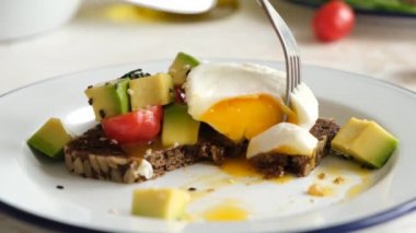Çatal ve bıçakla yumurtalı avokado tostu yemek. Kavrulmuş yumurta ve avokado salatasıyla gurme çavdar ekmeği yerken yakın çekim görüntüsü.