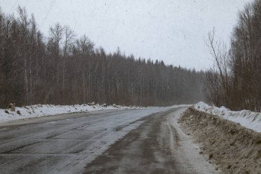 Eski bir çift şeritli yol, kaldırımda kirli kar dağları, yoğun kar yağışı..