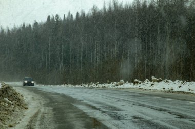 Eski iki şeritli bir otoyolda bir kesişme kötü havadan geçer. Yol kenarındaki kirli kar dağları, yoğun kar yağışı. Tekerleklerin altından su ve kar damlaları
