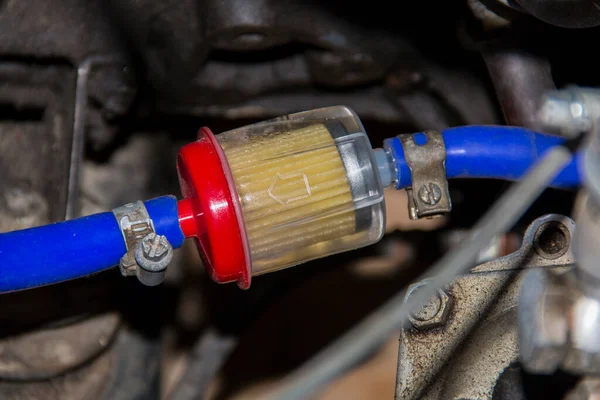 A transparent flowing fuel filter is installed in the gas line of the engine power system. Blue hoses are connected to the filter.