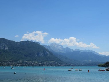 Dağlar, mavi gökyüzü ve Annecy Gölü 'nün arkasında beyaz bulutlar.
