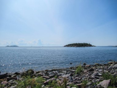 Deniz manzaralı kayalar, çimenler, mavi gökyüzü ve ufukta kabarık bulutlar.