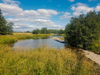 Güneşli bir günde, küçük bir şelalenin nehri ve üst tarafında beyaz bulutlar var..