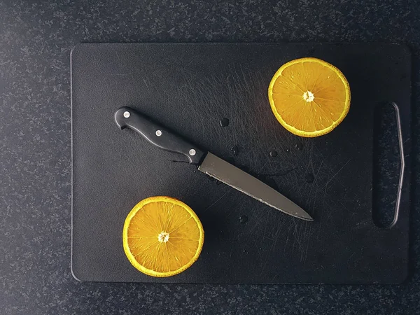 切碎的橙子和刀片在黑色切碎板上的成分 图库照片
