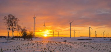 yel değirmenleri (rüzgar türbinleri) gün batımında karla kaplı sahada