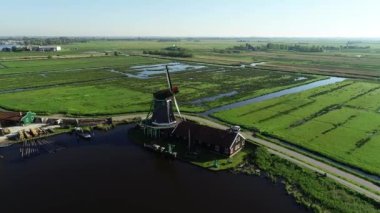 Zaanse Schans 'ın tarihi yel değirmenlerinin, Zaandijk ve Amsterdam' ın yakınlarındaki Zaandam 'ın insansız hava aracı görüntüsü. Bahar ya da yaz aylarında güneşli bir gün. Ördekler uçuyor, insanlar bisiklet sürüyor.