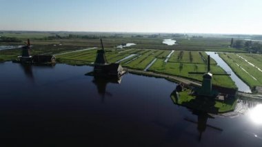 Zaanse Schans 'ın tarihi yel değirmenlerinin, Zaandijk ve Amsterdam' ın yakınlarındaki Zaandam 'ın insansız hava aracı görüntüsü. Bahar ya da yaz aylarında güneşli bir gün. Ördekler uçuyor, insanlar bisiklet sürüyor.