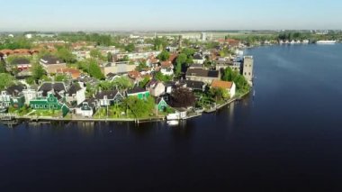 Zaanse Schans 'ın tarihi yel değirmenlerinin, Zaandijk ve Amsterdam' ın yakınlarındaki Zaandam 'ın insansız hava aracı görüntüsü. Bahar ya da yaz aylarında güneşli bir gün. Ördekler uçuyor, insanlar bisiklet sürüyor.