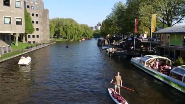 アムステルダム オランダ 6月2019 人々はアムステルダムの運河の川でウォータースポーツをしています 背景に都市とハイネケン博物館のパノラマビュー ボートに乗っている人は楽しい時間を過ごしている — ストック動画