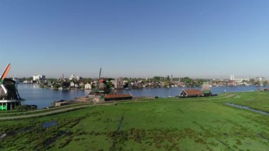 Zaanse Schans 'ın tarihi yel değirmenlerinin, Zaandijk ve Amsterdam' ın yakınlarındaki Zaandam 'ın insansız hava aracı görüntüsü. Bahar ya da yaz aylarında güneşli bir gün. Ördekler uçuyor, insanlar bisiklet sürüyor.