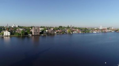 Zaanse Schans 'ın tarihi yel değirmenlerinin, Zaandijk ve Amsterdam' ın yakınlarındaki Zaandam 'ın insansız hava aracı görüntüsü. Bahar ya da yaz aylarında güneşli bir gün. Ördekler uçuyor, insanlar bisiklet sürüyor.