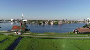 Zaanse Schans 'ın tarihi yel değirmenlerinin, Zaandijk ve Amsterdam' ın yakınlarındaki Zaandam 'ın insansız hava aracı görüntüsü. Bahar ya da yaz aylarında güneşli bir gün. Ördekler uçuyor, insanlar bisiklet sürüyor.