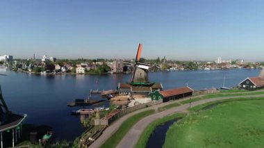 Zaanse Schans 'ın tarihi yel değirmenlerinin, Zaandijk ve Amsterdam' ın yakınlarındaki Zaandam 'ın insansız hava aracı görüntüsü. Bahar ya da yaz aylarında güneşli bir gün. Ördekler uçuyor, insanlar bisiklet sürüyor.
