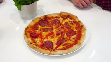 Beyaz bir masada, pizzacıda oturan arkadaşlar İtalyan usulü lezzetli pizzalar yiyorlar. Yemek paylaşımı, arkadaşlarla vakit geçirmek, İtalyan yemeği, taze pişmiş pizza.