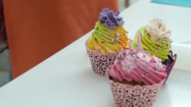 Kadının elinin yakın çekimlerinde taze, nefis, renkli kremalı bir kek var ve onu masaya koyuyor. Taze kek ister misin? Konsept: fırın, şekerci, çalışan kadınlar