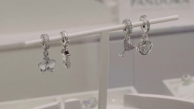 In a jewelry shop: Sparkling silver charms with glittering stones and crystals hanging and swinging on hanger, on white background in jewelry shop, slow motion. Beautiful luxury jewelry