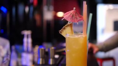 Bir bar tezgahında, avuç içi ve ananaslı renkli bir içecek. Kulüp içi, insanlar harika zaman geçiriyor..