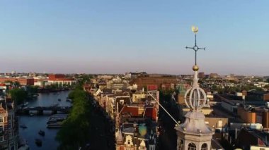 Hollanda, Amsterdam 'daki ünlü yerlerin hava manzarası, bahar veya yaz günbatımında. Kanal ve eski merkez bölgenin üzerinde uçuyor. Arka planda Munttoren Çan Kulesi var. Güzel sıcak renkler