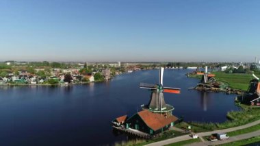 Zaanse Schans, Zaandijk ve Amsterdam Hollanda yakınlarındaki Zaandam 'ın tarihi yel değirmenlerinin insansız hava aracı görüntüsü. Bahar ya da yaz aylarında güneşli bir gün, sabah güneşi. Ördekler uçuyor, insanlar bisiklet sürüyor.