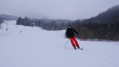 Profesyonel kayakçı yamaçtan aşağı kayıyor. Güzel beyaz kış manzarası, karla kaplı ağaçlar. Kayakçı klasik kayak stilinde hızlı gidiyor..