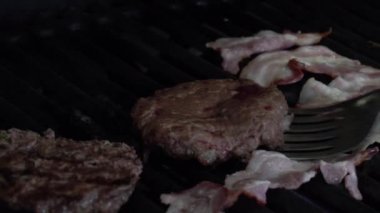 Hamburgerler ızgarada kızarıyor. Izgarada iki lezzetli görünümlü hamburger kızartması. Ateş cızırdıyor, alevler çıkıyor.