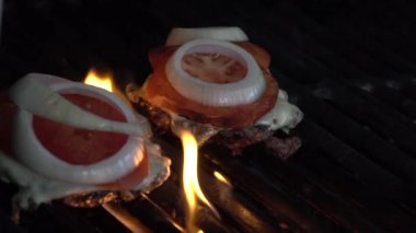 Hamburgerler ızgarada kızarıyor. Izgarada iki lezzetli görünümlü hamburger kızartması. Ateş cızırdıyor, alevler çıkıyor.