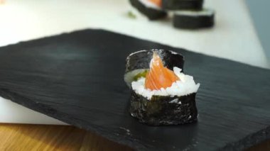 Suşi ustası Japon restoranında taze ve lezzetli suşi ruloları hazırlıyor ve tabağa koyuyor. Konsept: bambu matında suşi rulosu yapmak. Suşi yapmak, malzemeleri kesmek.