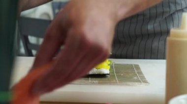 Sushi master preparing fresh and tasty sushi rolls in Japanese restaurant. Concept: Rolling a sushi roll on bamboo mat.Sushi making process, cutting ingredients