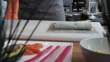 Suşi ustası Japon restoranında taze ve lezzetli suşi ruloları hazırlıyor ve tabağa koyuyor. Konsept: bambu matında suşi rulosu yapmak. Suşi yapmak, malzemeleri kesmek.