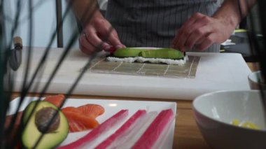 Suşi ustası Japon restoranında taze ve lezzetli suşi ruloları hazırlıyor. Kavram: avokadoyla bambu hasırında suşi rulosu yapmak. Suşi yapma süreci, malzemeleri kesme.